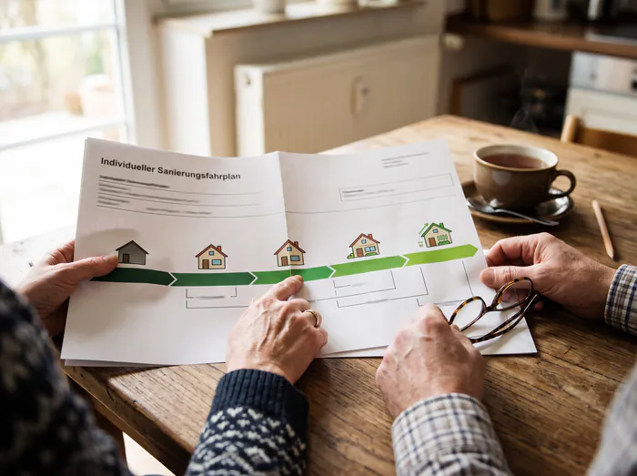 Hausbesitzerpaar hält den aufgeklappten Sanierungsfahrplan in den Händen: fünf Etappen vom unsanierten zum sanierten Haus